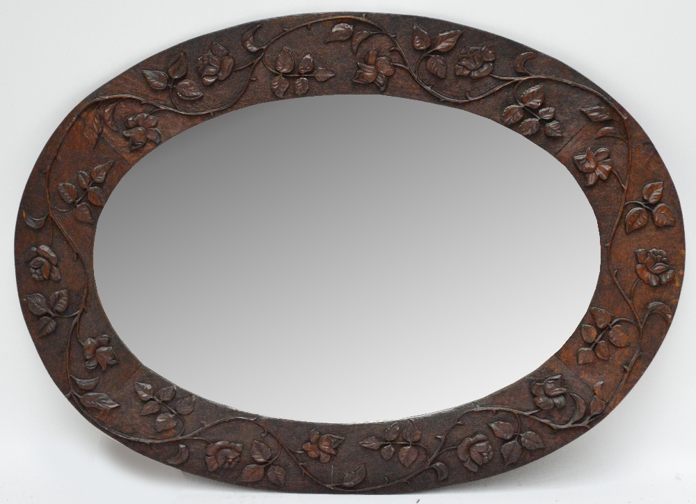 MACCLESFIELD SCHOOL OF CARVING; a carved oak framed wall mirror decorated with roses, the bevelled