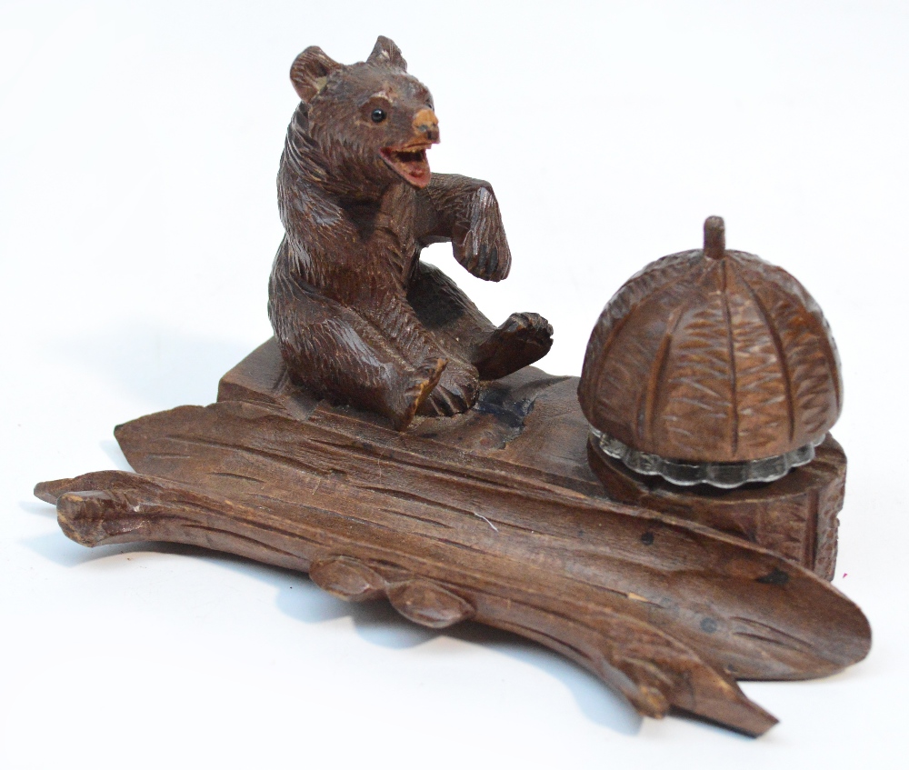 A late 19th century Black Forest carved inkstand modelled as a seated bear before the glass well
