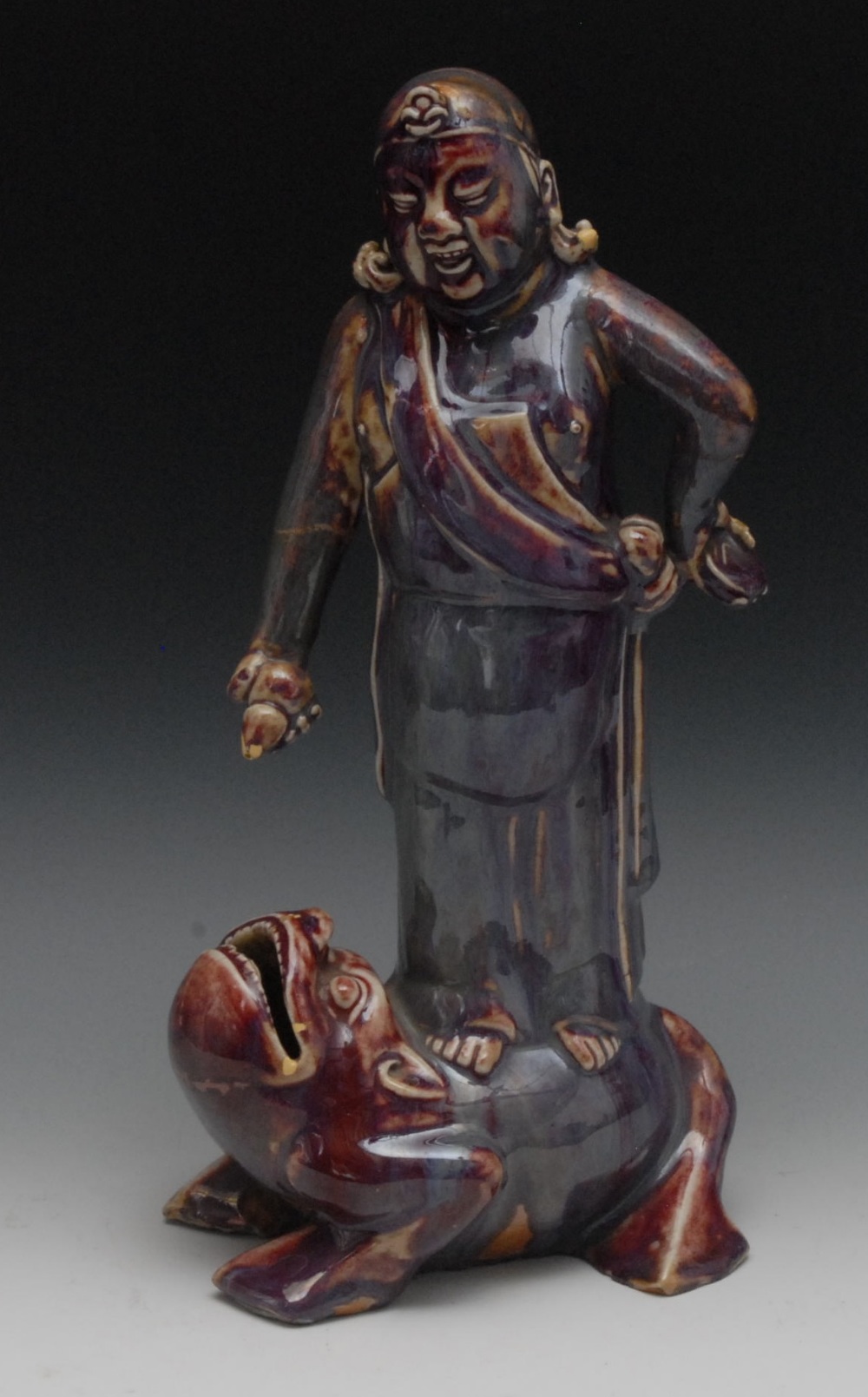 A Chinese monochrome figure, of Liu Hai, standing on the back of the three-legged toad, glazed in