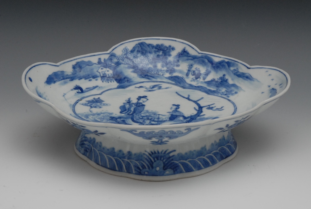 A Chinese quatrefoil pedestal dish, decorated in underglaze blue with two figures and a dog in a log