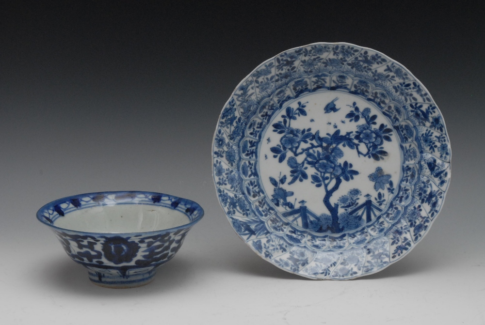 A Chinese shaped circular plate, painted in underglaze blue with stylised tree and fence, the rim