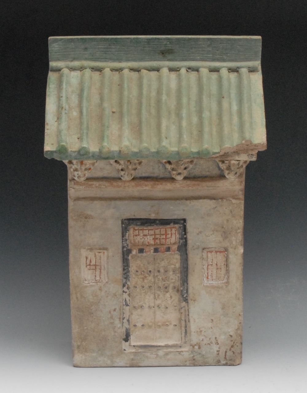 A Chinese pottery model of a house, with a ridged sloping roof and a door flanked by square windows,