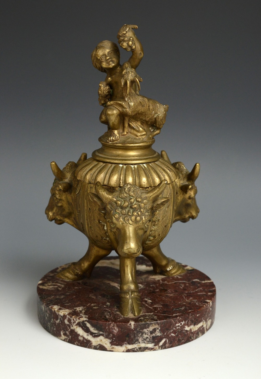 A 19th century bronze inkwell, cast with acanthus and three bulls` heads, the cover surmounted by