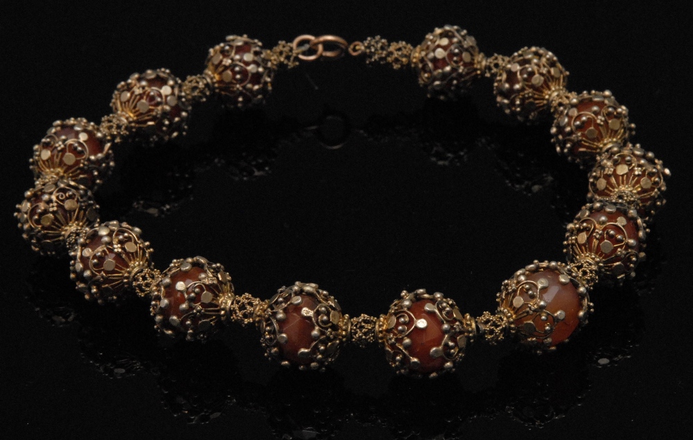 A gilt filigree mounted carnelian necklace, the fourteen facetted beads encased in scrollwork