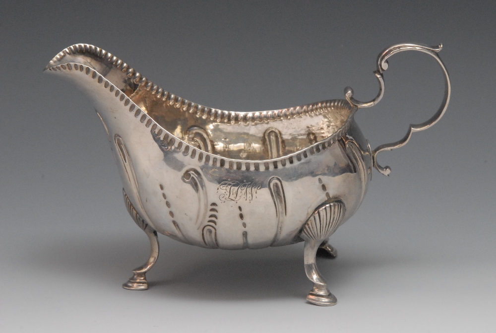 A George III Irish sauce boat, flying scroll handle, punch decorated rim, shell scroll legs and