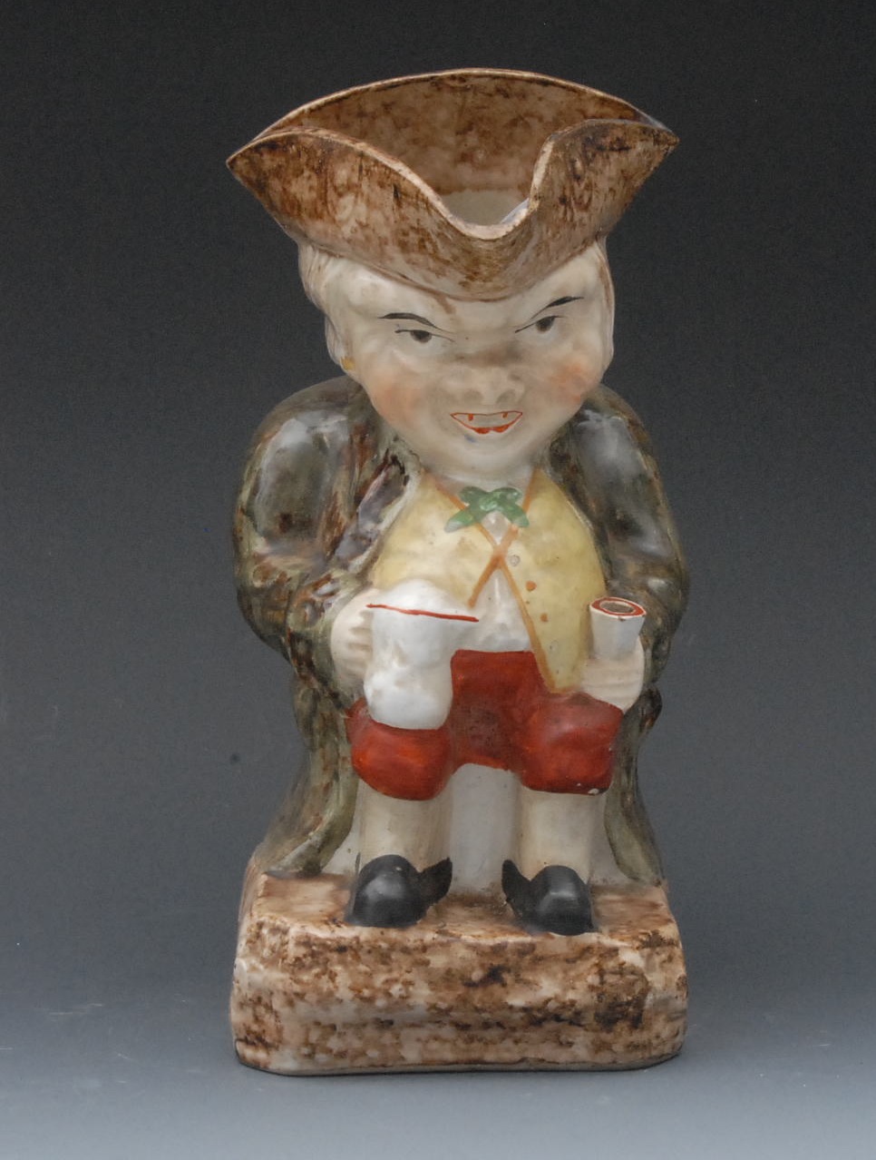 A 19th century toby jug, he sits, wearing a tricorn hat, a jug and an ale glass, canted square base,
