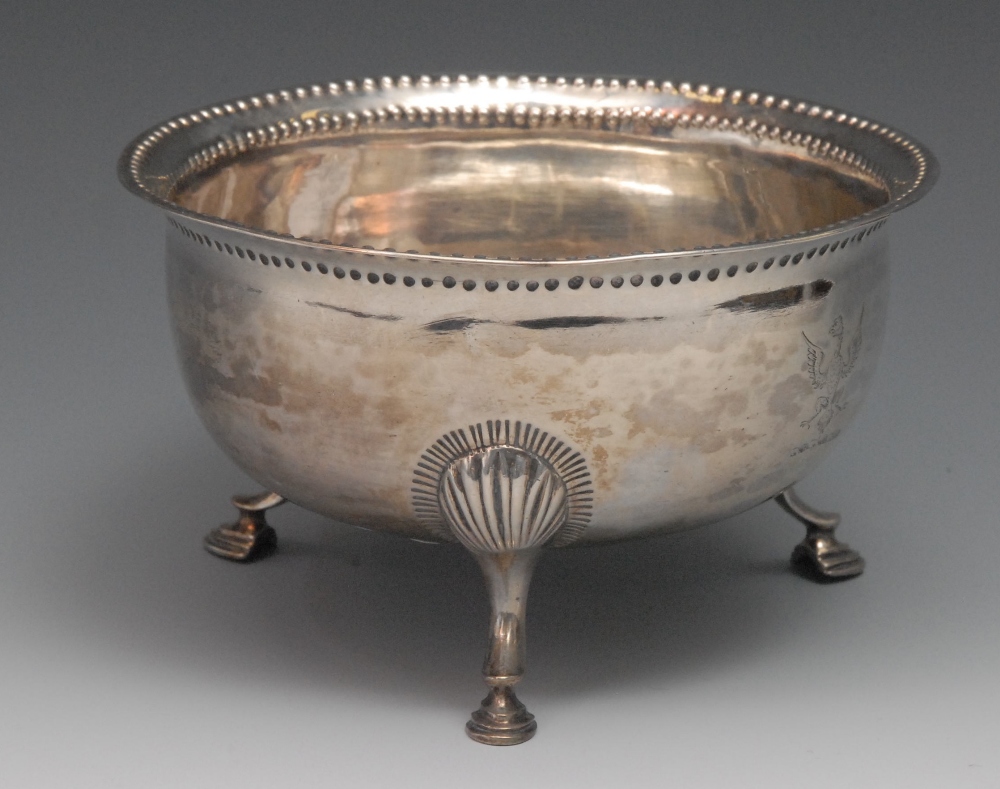 A George III Irish bowl, engraved armorial, punch decorated rim, shell scroll legs and pad feet,