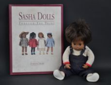 A Sasha baby doll, vinyl head and body, airbrushed detail to face, brown wig, appropriately dressed,