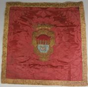A red damask and embroidered chair back centered with a coat of arms enclosed in a bullion border,
