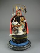 An early 20th Century pedlar doll under glass dome, the moulded painted face with black cape and