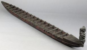 A model of a Maori canoe (waka), the hull carved with lines and Tiki masks with sixteen chip