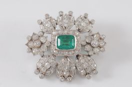 An emerald and diamond mounted oval brooch with central ‘emerald-cut ‘ emerald approximately 6.5mm x