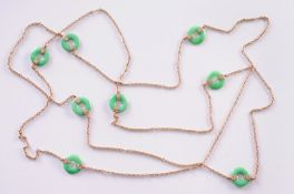 An early 20th century gold and jade disc long chain, of trace and twist linking, interspersed with