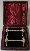 A pair of Victorian plated knife rests contained in a fitted case.