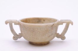 A Chinese jade two handled cup of archaic form, with bands of roundel’s and shaped handles on a