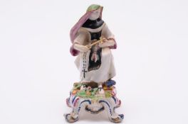 A Bow figure of a nun wearing a black, green and pink habit and headdress, holding a cross, on mound