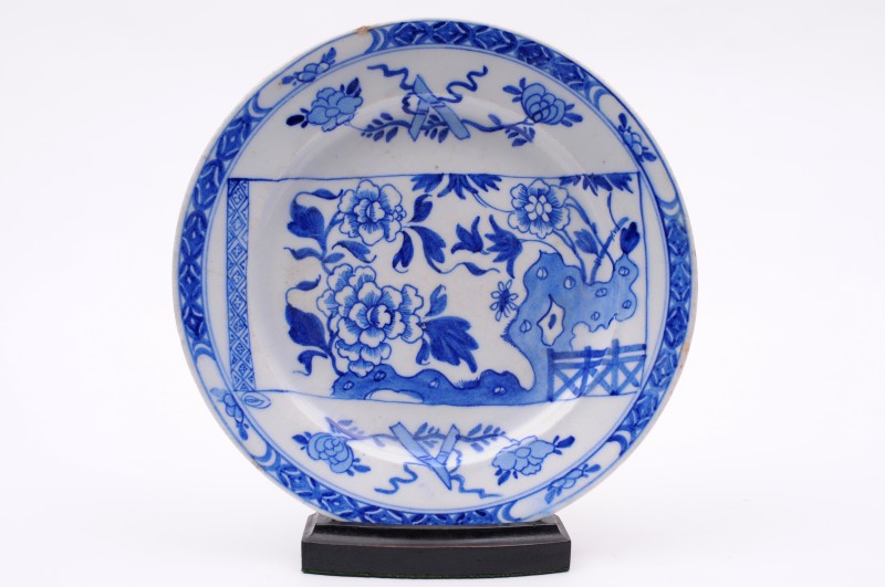 A Bow blue and white plate painted with a central scroll panel of flowers, rockwork and a fence, the