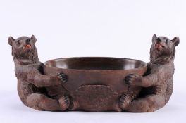 A Swiss carved linden wood Black Forest bowl of oval outline held by two seated bears, with