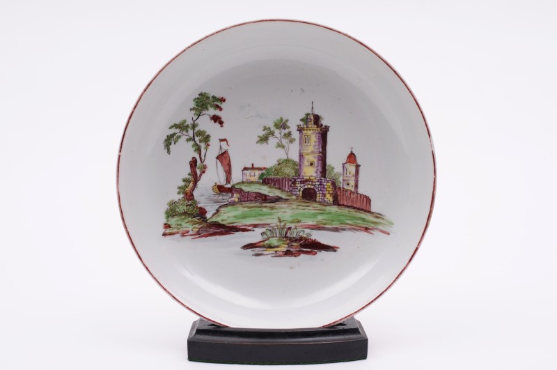 A Longton Hall saucer dish painted in ‘Castle Painter’ style with a fortified tower, a church