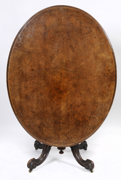 An oval walnut tilt top table, on a carved base, 136 cm wide  See illustration