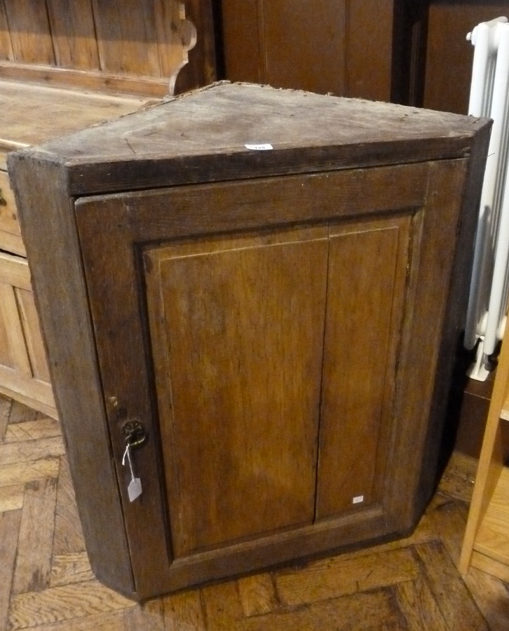 A modern pine wall hanging corner cupboard with panelled door, enclosing a three shelved interior,