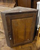 A modern pine wall hanging corner cupboard with panelled door, enclosing a three shelved interior,