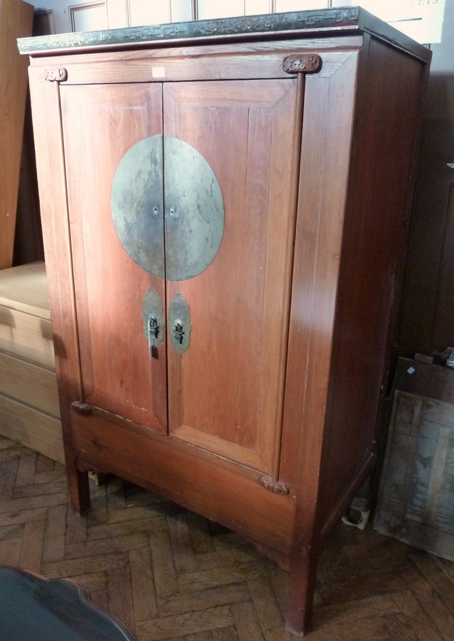 A modern hardwood oriental style cupboard with carved frieze , panelled doors, with metal mounts,