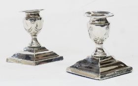 Pair Edwardian squat candlesticks, urn shaped, decorated with swags on tapered square bases,