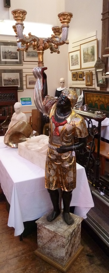 A carved and painted blackamoor, standing holding gilt and silver painted candelabrum, in heavily