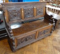 An oak monk's bench, heavily carved with lion masks, lion mask panels to back and carved phoenix