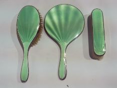 A three piece green enamel and silver backed dressing table set comprising hairbrush, hand mirror