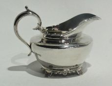 A George IV silver cream jug of plain compressed form with scroll handle, raised on cast foliate