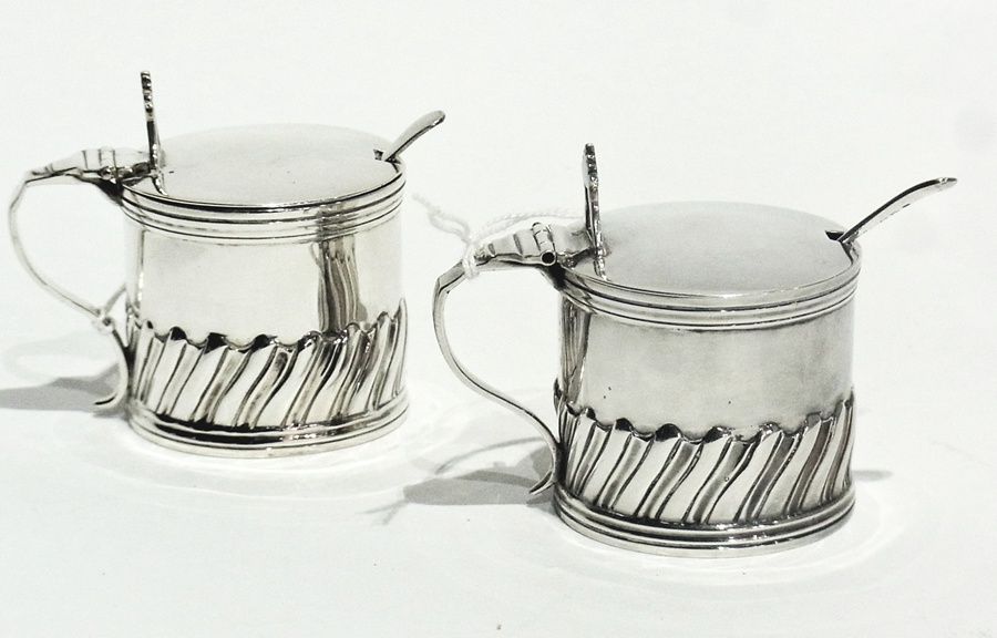 A pair of Victorian silver mustard pots with hinged tops and glass liners, and spoons, London
