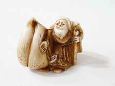 Japanese carved ivory netsuke, in the form of a sage with closed lotus flower, 2.5cm high, signed to