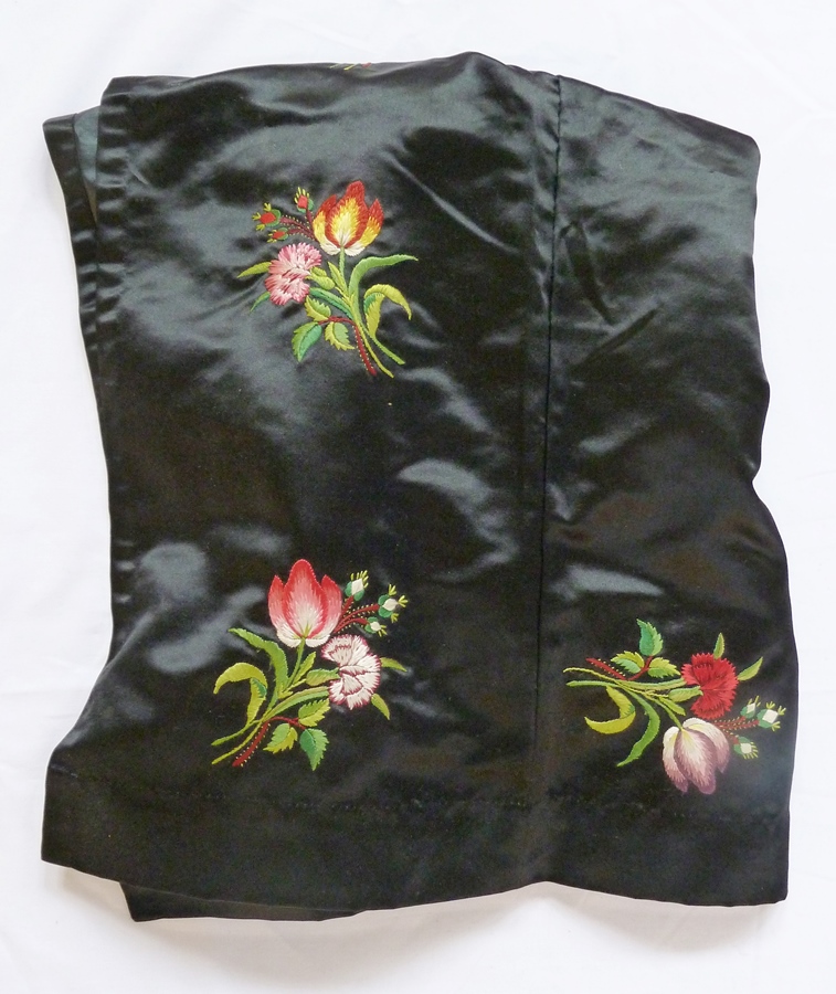 A Victorian black satin "dress" apron, embroidered with tulips and carnations in bunches, pockets