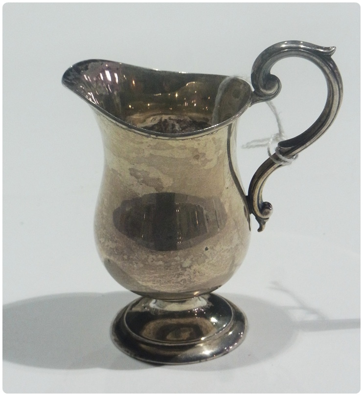 A George V silver cream jug, of plain form, with scroll handle, raised on a circular foot,