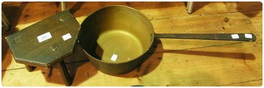 An old brass saucepan with a long iron handle, and a three legged milking stool