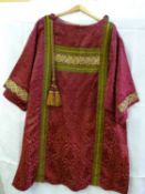 A red silk vestment with gold thread embroidery in panels with tassels and silk covered buttons