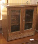 An early twentieth century oak smoker's cabinet, the pair of bevelled glass doors enclosing fitted