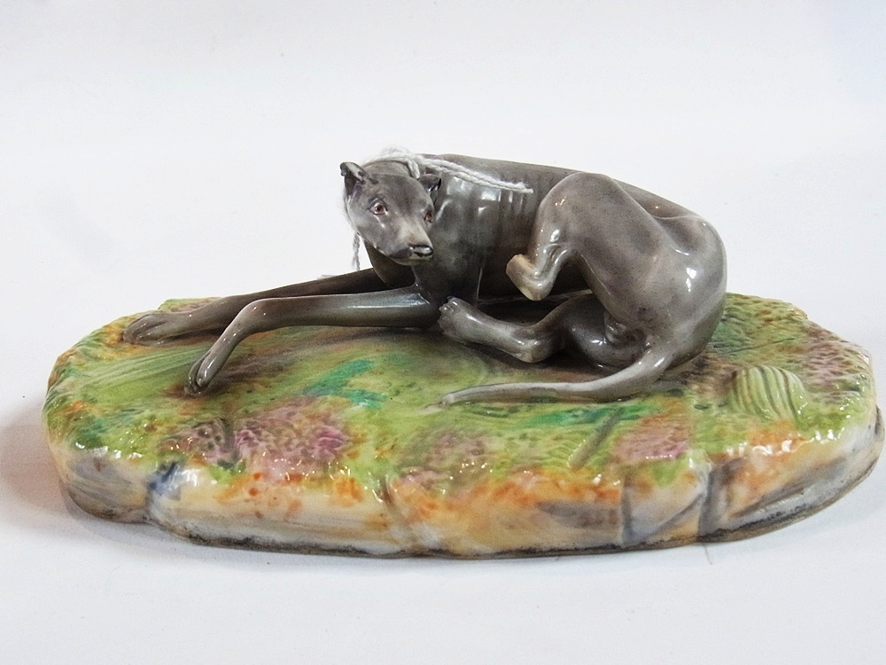 Porcelain figure of a greyhound, lying on an oval plinth (af), length 16cm