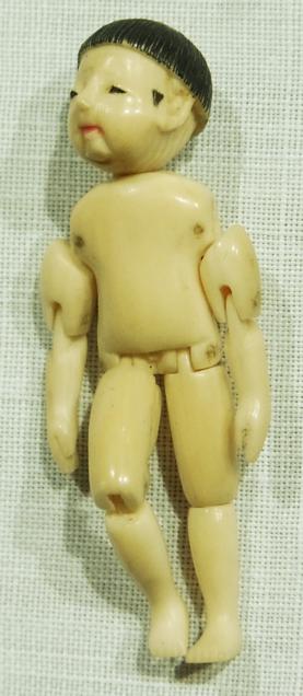 A miniature ivory doll with jointed arms and legs and pips, with a painted face in the oriental