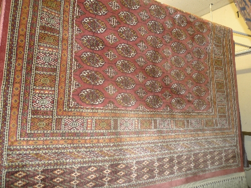 A Persian design Bokhara rug the rose coloured field with repeated motifs within a geometric border