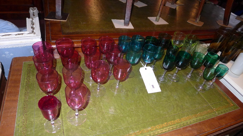 A collection of cranberry glass and green glass drinking glasses together with coloured glass