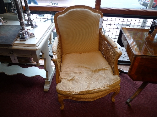 A pair of French style bergere armchairs upholstered in gold fabric with cane panel sides