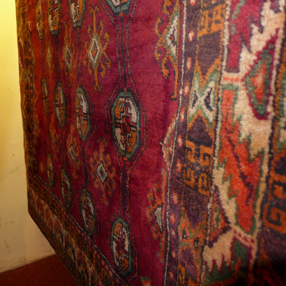 A hand knotted Persian Bokhara carpet the red field with repeated motifs within a stylized border