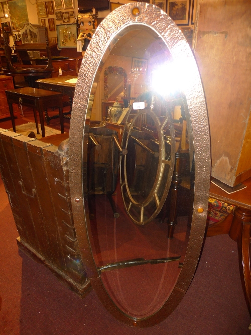 An Arts and Crafts mirror the oval bevelled plate in copper clad frame