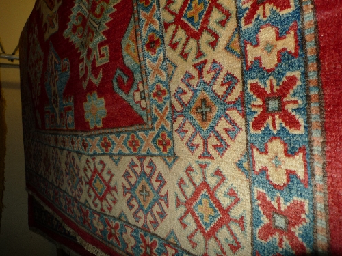 A fine Kazak rug with twin pole medallion on a rouge field within repeating sapphire geometrical