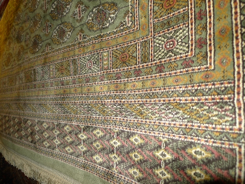 A hand mottled Persian Belouch rug the green field with repeated motifs within a stylized border