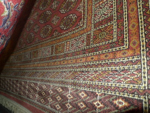 A hand knotted Persian Bokhara rug the rose coloured field with repeated motifs within a stylized