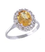A yellow sapphire and diamond cluster ring, the oval cut sapphire within a surround of brilliant